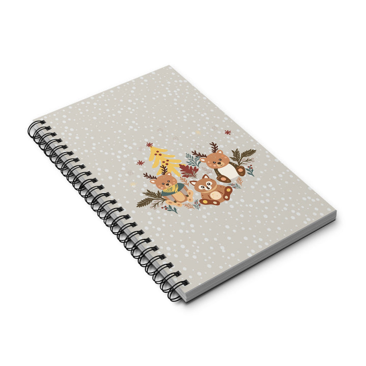 A spiral-bound notebook with a light gray cover decorated with small white speckles and a central illustration of woodland animals including a deer, bear, fox, and bird with autumn foliage.