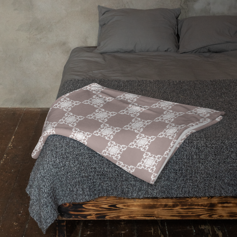 Picture of an earth tone mauve throw blanket sitting across the end of a bed. It's super cute
