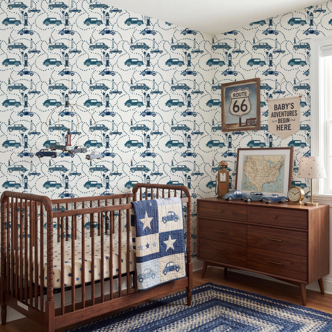 A styled nursery room featuring a wooden crib and dresser, decorated with blue and white car-patterned wallpaper, a blue quilt, and vintage-style wall signs.