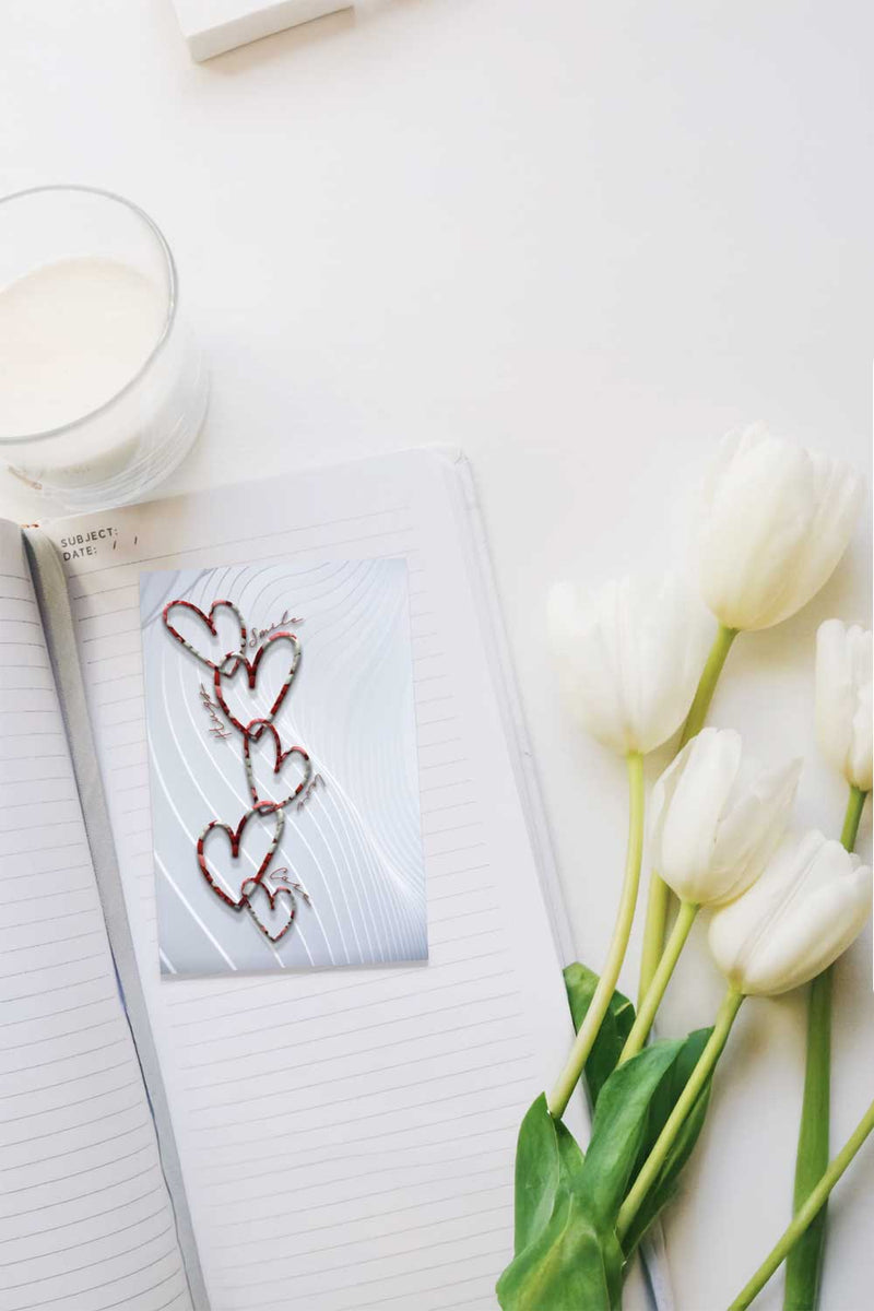White tulips next to a glass of milk and a book with a bookmark with heart designs on a white surface