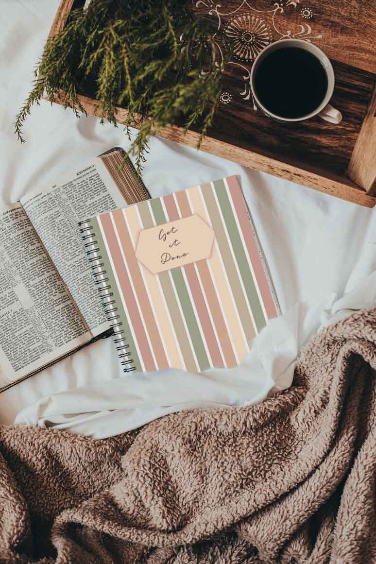 This is a picture of the Dig'n Designs Planner Journal sitting on a bed with an open book and drink